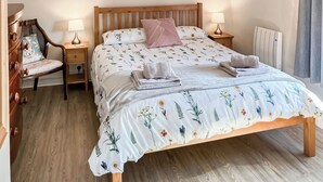 Un lit bien fait, avec une literie à motifs floraux, une tête de lit en bois et une table de chevet sur laquelle se trouve une lampe.