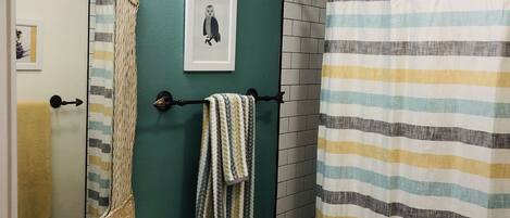 A bathroom with a white sink, a toilet, a striped shower curtain, and a mirror with a woven frame.