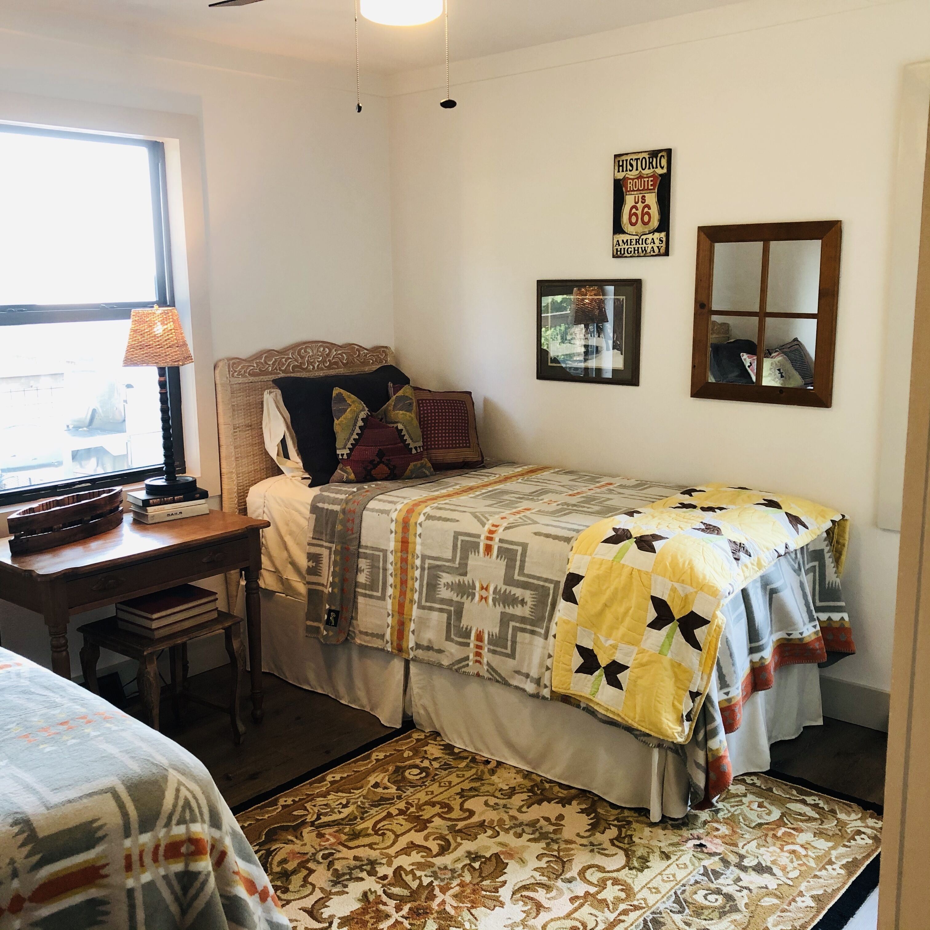 Een slaapkamer met een bed, een bureau, een lamp, een raam en een spiegel en bord aan de muur.