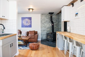 Una cocina con estufa de leña, un comedor con taburetes de bar y una sala de estar con sofá y un elemento decorativo en la pared.