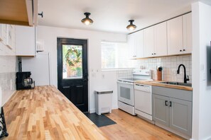 Una cocina moderna con armarios blancos, encimera de madera, puerta negra y una ventana con persianas.