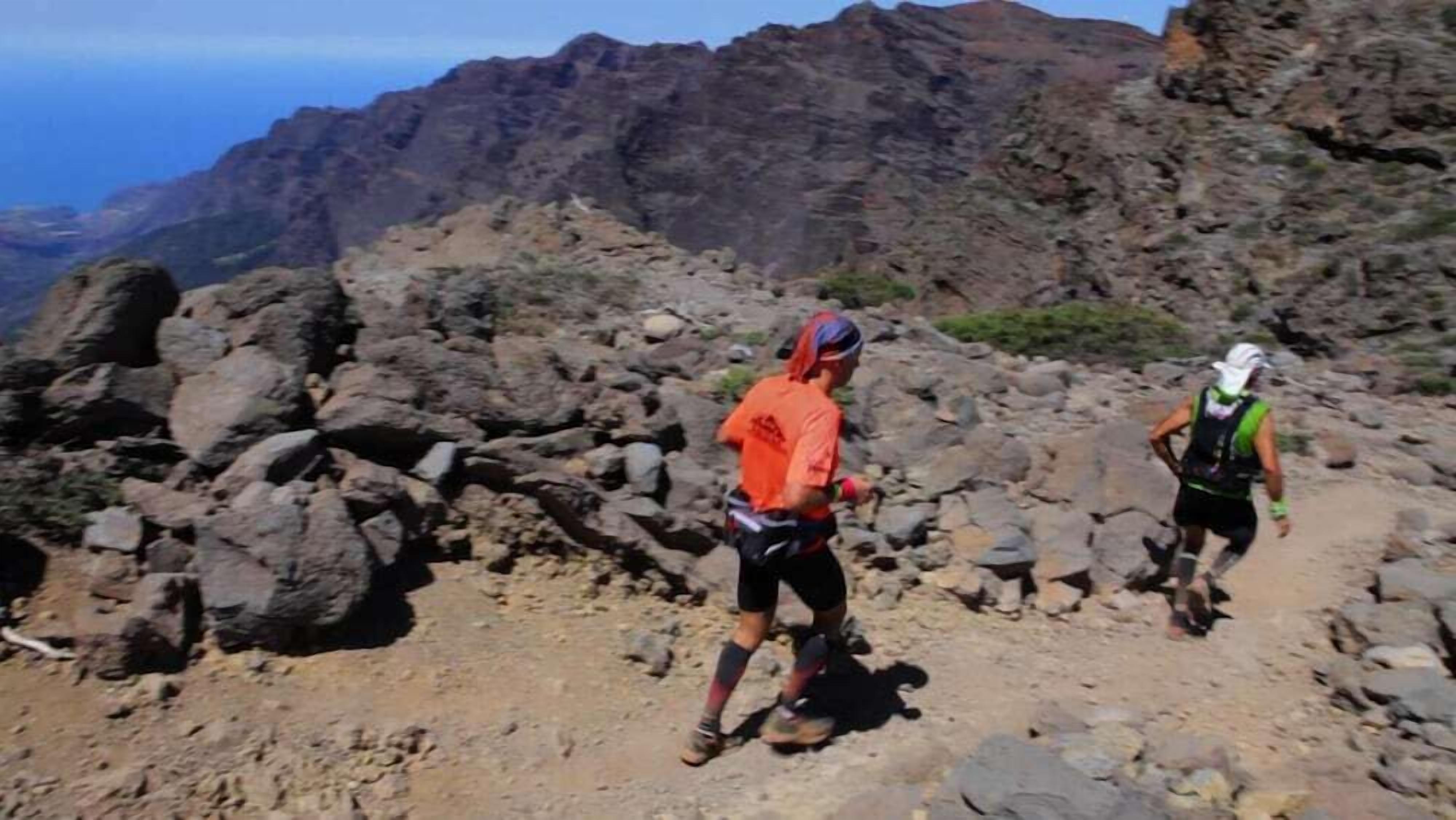 Two hikers on a rocky trail with a mountainous backdrop.