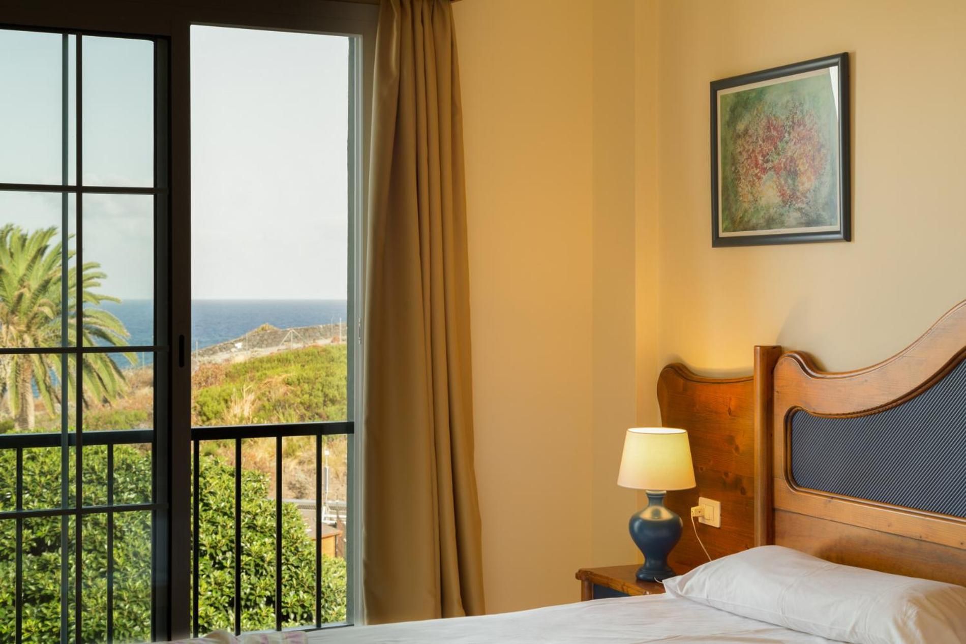 Une chambre d’hôtel dotée d’une grande fenêtre donnant sur l’océan et la verdure.