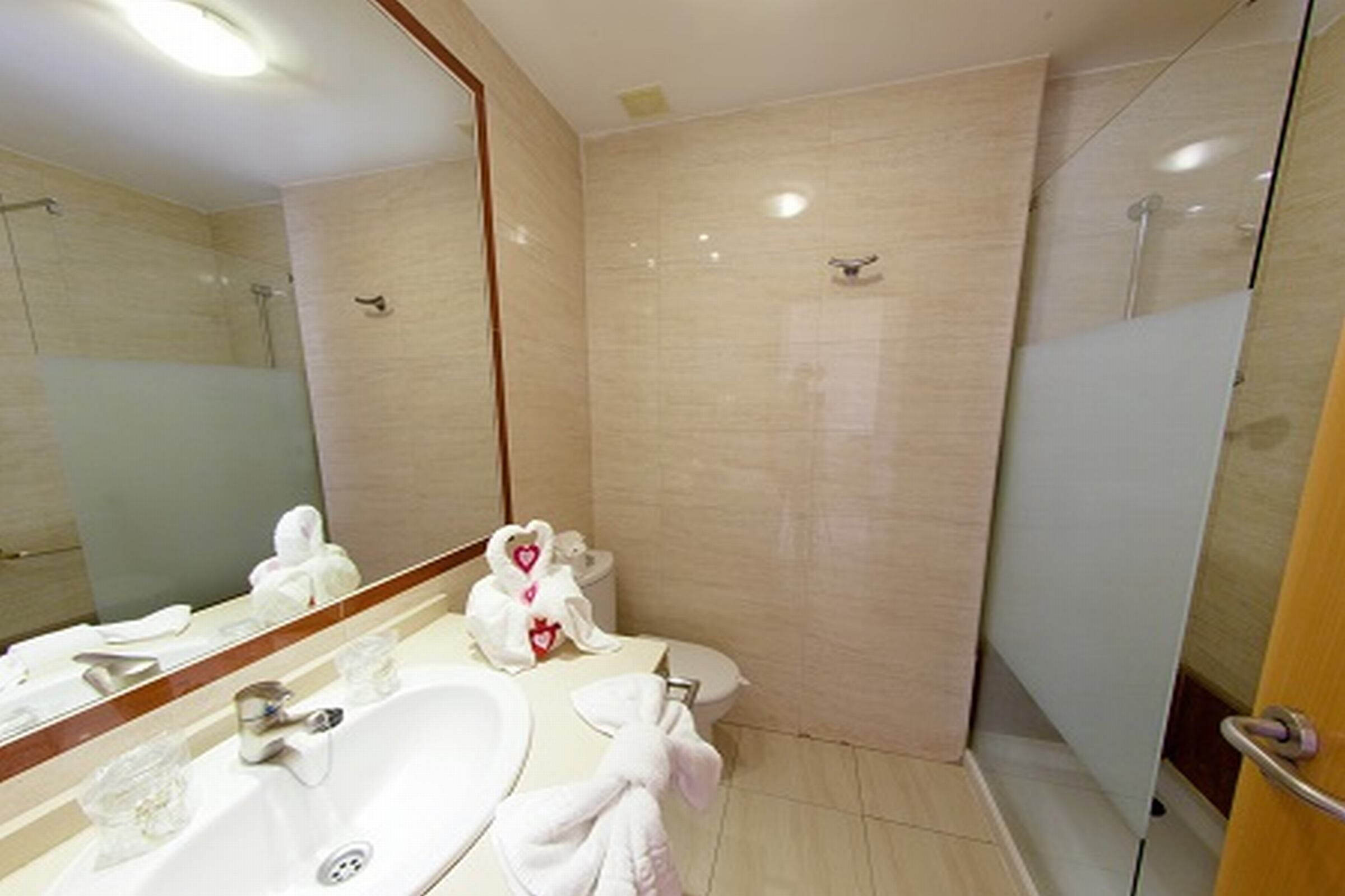 A bathroom with a large mirror, a sink, a toilet, and a shower area.