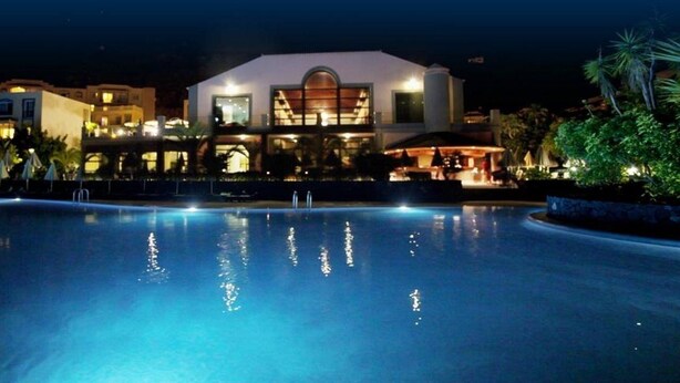 A nighttime view of a hotel with a swimming pool, a bar area, and a large building with a prominent arched window. - Hotel Las Olas (Brena Baja)