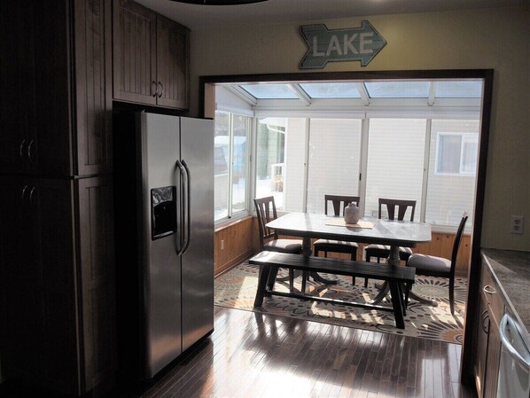 A kitchen with a stainless steel refrigerator, wooden cabinets, a dining table with chairs, and a view of a backyard through a glass door.