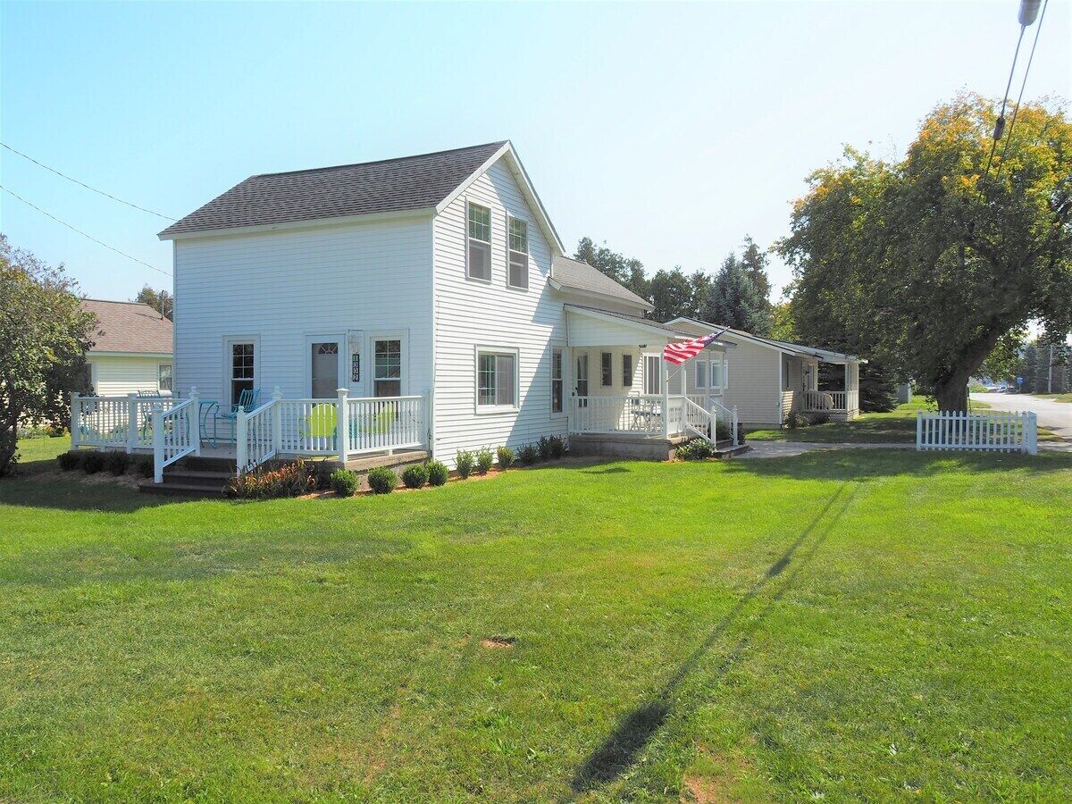 A two-story white house with a front porch, a small garden, and a flag.