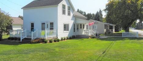 A two-story white house with a front porch, a small garden, and a flag.