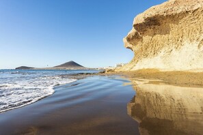 Una playa con una gran formación rocosa y una montaña al fondo.