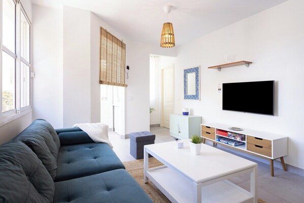 A modern living room with a blue sofa, a white coffee table, and a TV on a white cabinet.