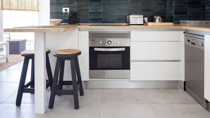 Una cocina moderna con armarios blancos, horno empotrado, lavavajillas y encimera de madera. Hay dos taburetes en la isla de la cocina.