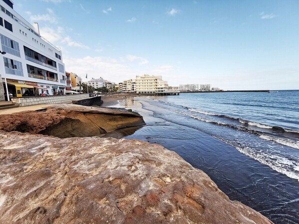 A coastal hotel with a rocky shoreline, a pier extending into the sea, and a clear sky.