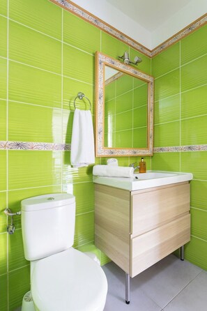 A bathroom with green tiles, a white toilet, a wooden vanity with a mirror, and a white sink.