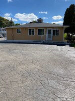 Un edificio pequeño de un solo piso con un letrero que dice 'OFFICE', una entrada frontal con escalones y un estacionamiento al frente.
