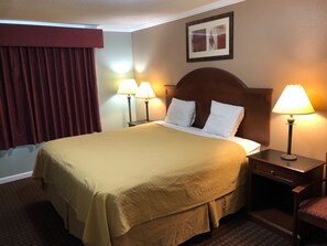 A hotel room with a large bed, two bedside lamps, a wooden headboard, a red curtain, and a framed picture on the wall.