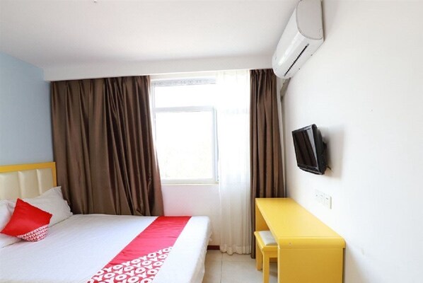 Una habitación de hotel con cama, escritorio, televisor y ventana con cortinas.