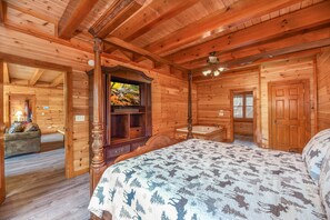 Ein Holzblockhaus-Innenraum mit einem Bett, einem Holzkasten, einem Fernseher und einem Badezimmer.