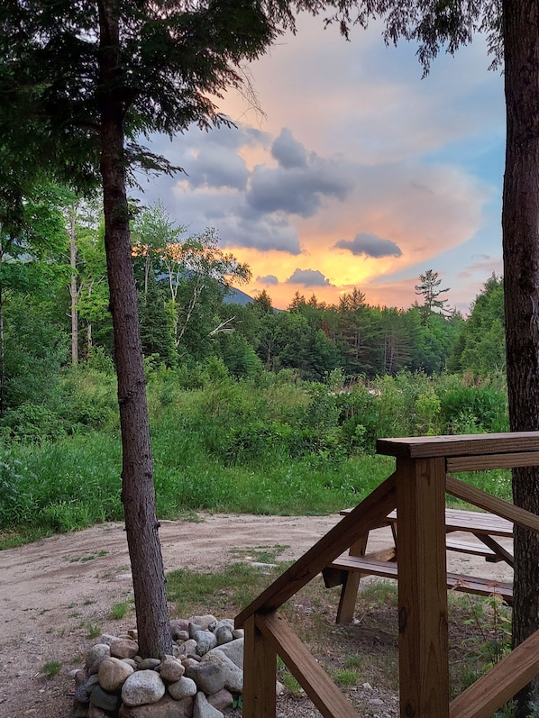 A wooden deck with a view of a forest and a sunset.