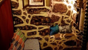 Ein raum mit Steinwänden, einem Holzregal, einer hängenden Leuchte und einem gemusterten Kissen.