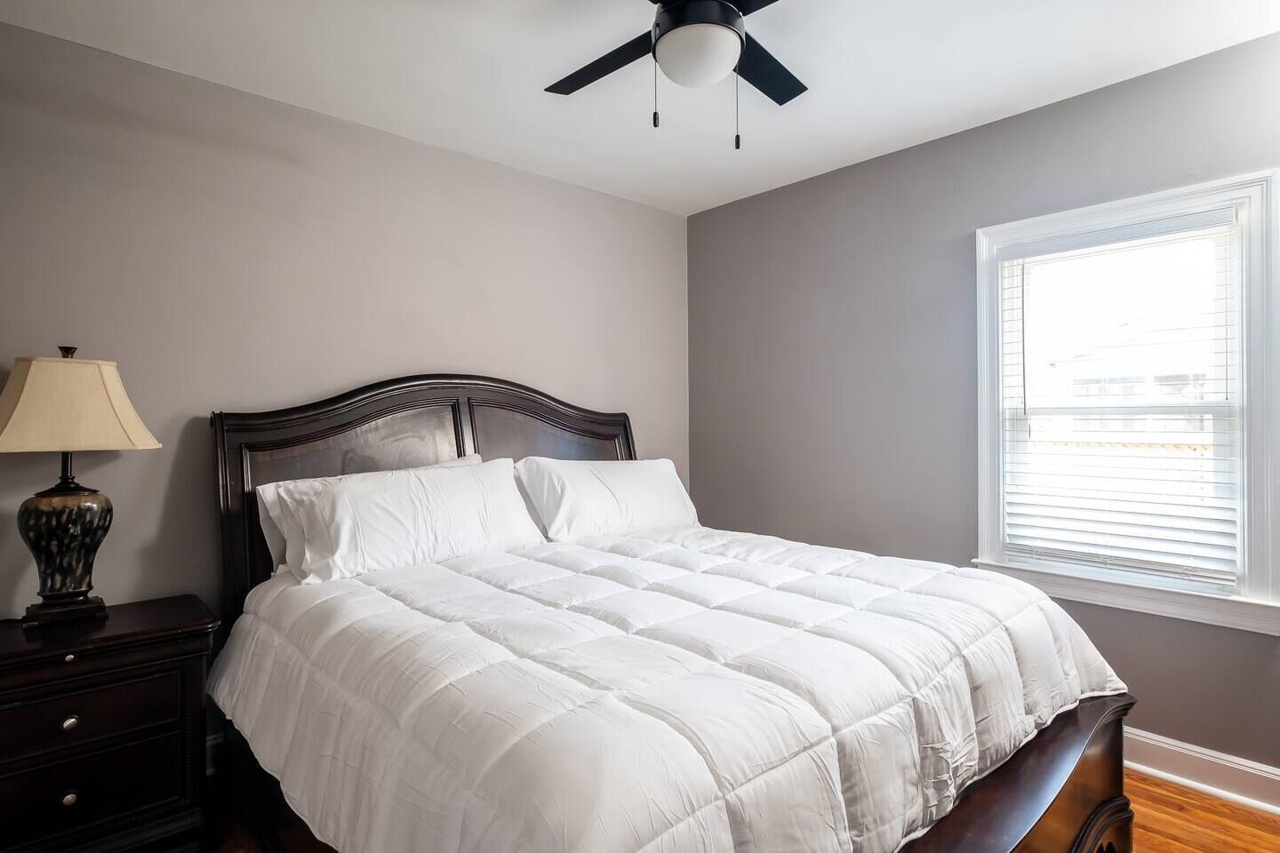 A bedroom with a bed, a nightstand, a lamp, a ceiling fan, and a window.