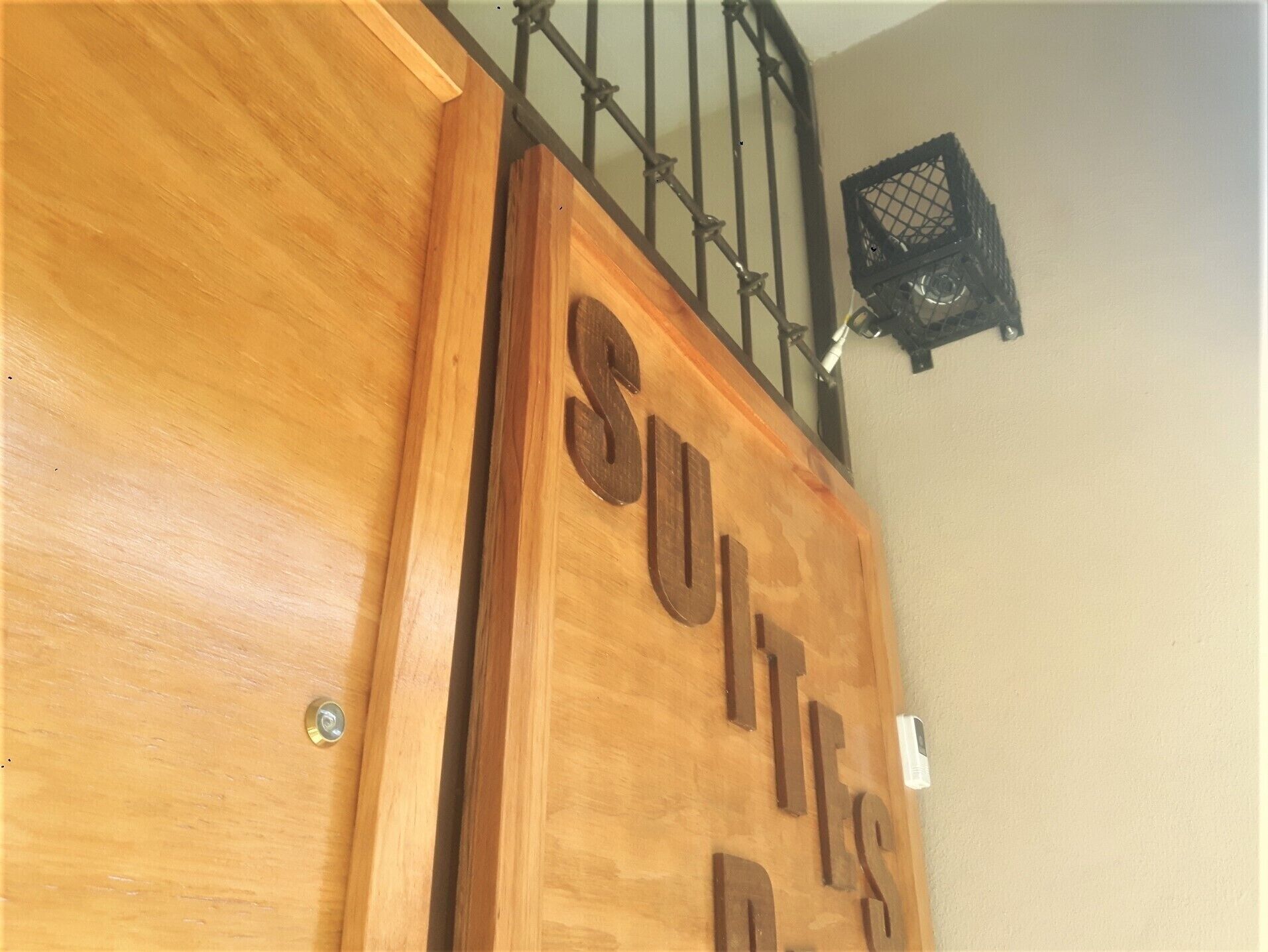 A wooden sign with the text "Suits Only" mounted on a wall near a staircase.