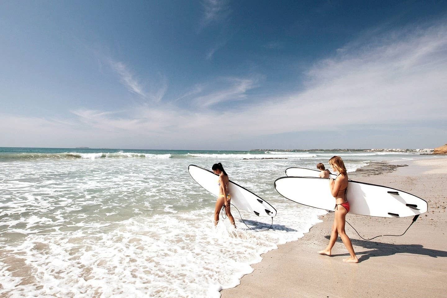 Une scène de plage où deux personnes, tenant des planches de surf, marchent le long du rivage.