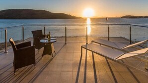 A terrace with chairs, a table, and a view of the sunset over water. - Hamilton Island Yacht Club Villas (Whitsundays)