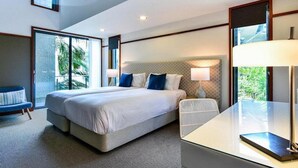 A modern hotel room with a large bed, a desk, and a view of greenery through the windows. - Hamilton Island Yacht Club Villas (Whitsundays)