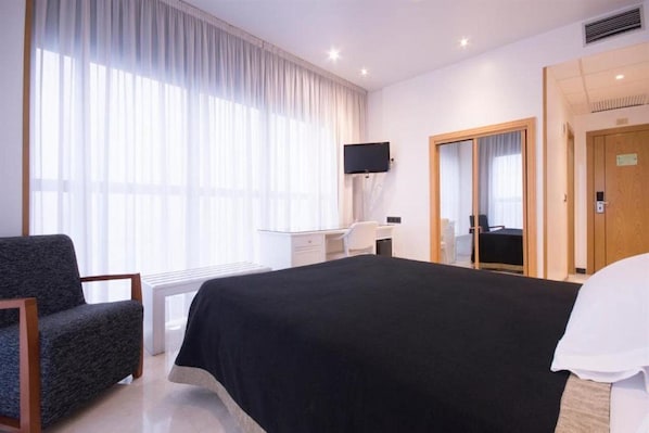 A hotel room with a bed, a desk, a chair, a TV, and a large window with curtains. - Santiago (Lugo)