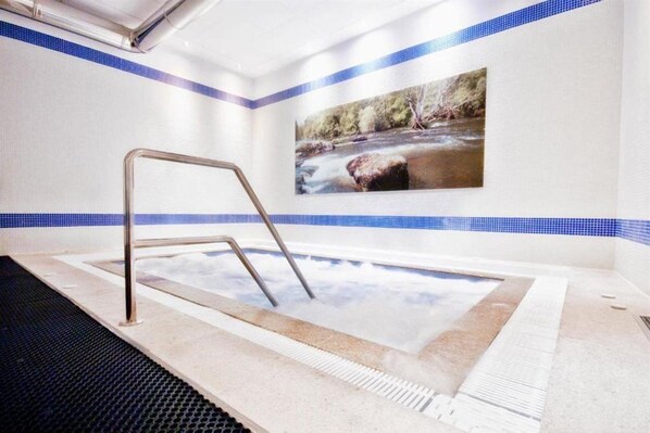 A hot tub with a metal ladder, surrounded by a tiled wall with a blue border and a picture of a river scene. - Santiago (Lugo)