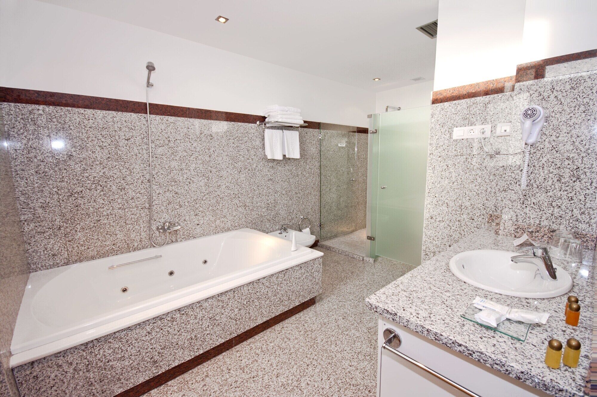 Un baño moderno con una bañera grande, una ducha con mampara de vidrio y una encimera de granito con lavamanos y mueble.