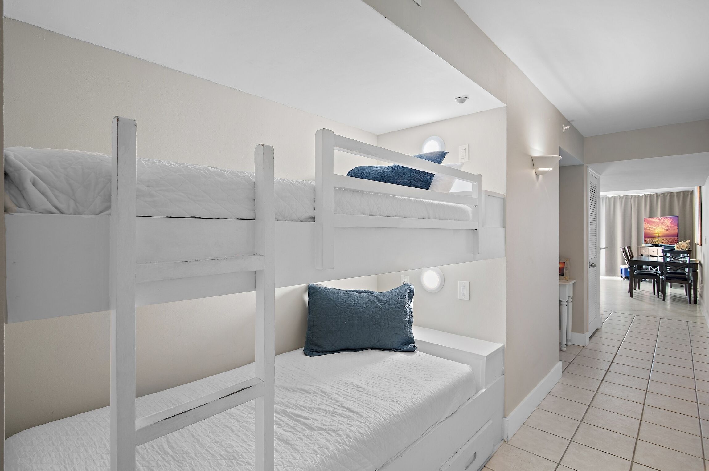 A bunk bed room with white bedding and a blue pillow.
