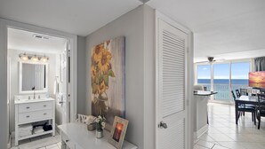 A bathroom with a white vanity, a large mirror, and a painting of sunflowers. - Pelican Beach Resort, Beachfront 7th floor , White Beach, Pool, WiFi, Cable TV (Destin)