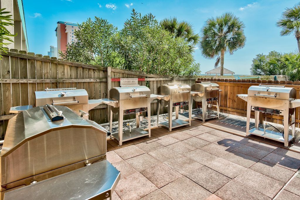 An outdoor patio with multiple barbecue grills and a wooden fence.