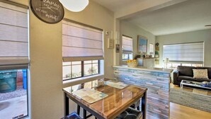 A dining area with a wooden table and chairs, a bar area with a counter, and a living room with a sofa and a coffee table. - Phoenix Home | Pool & String Lights (Phoenix)