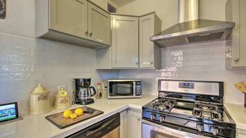 A kitchen with white cabinets, a stainless steel range hood, a microwave, a stove, and a dishwasher.