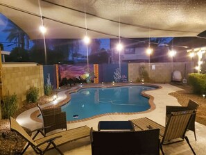 An outdoor swimming pool with a curved edge, surrounded by lounge chairs and a covered patio area.