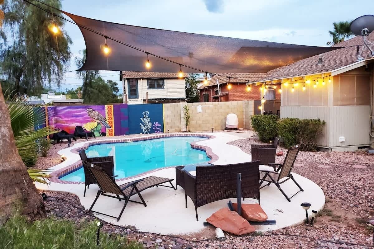 A backyard with a swimming pool, lounge chairs, and a barbecue area.
