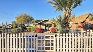 A residential property with a white picket fence, a palm tree, and a red flowering bush. - Phoenix Home | Pool & String Lights (Phoenix)