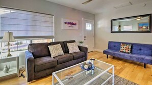 A living room with a brown sofa, a blue sofa, a glass coffee table, and a ceiling fan. - Phoenix Home | Pool & String Lights (Phoenix)