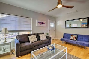 A living room with a brown sofa, a blue sofa, a glass coffee table, and a ceiling fan.