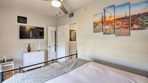 A bedroom with a bed, a ceiling fan, a TV, a dresser, and a door. - Phoenix Home | Pool & String Lights (Phoenix)