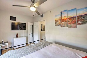 A bedroom with a bed, a ceiling fan, a TV, a dresser, and a door.