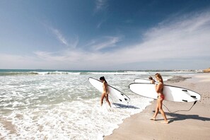 Et strandbillede med to personer, der bærer surfboards og går langs vandkanten.