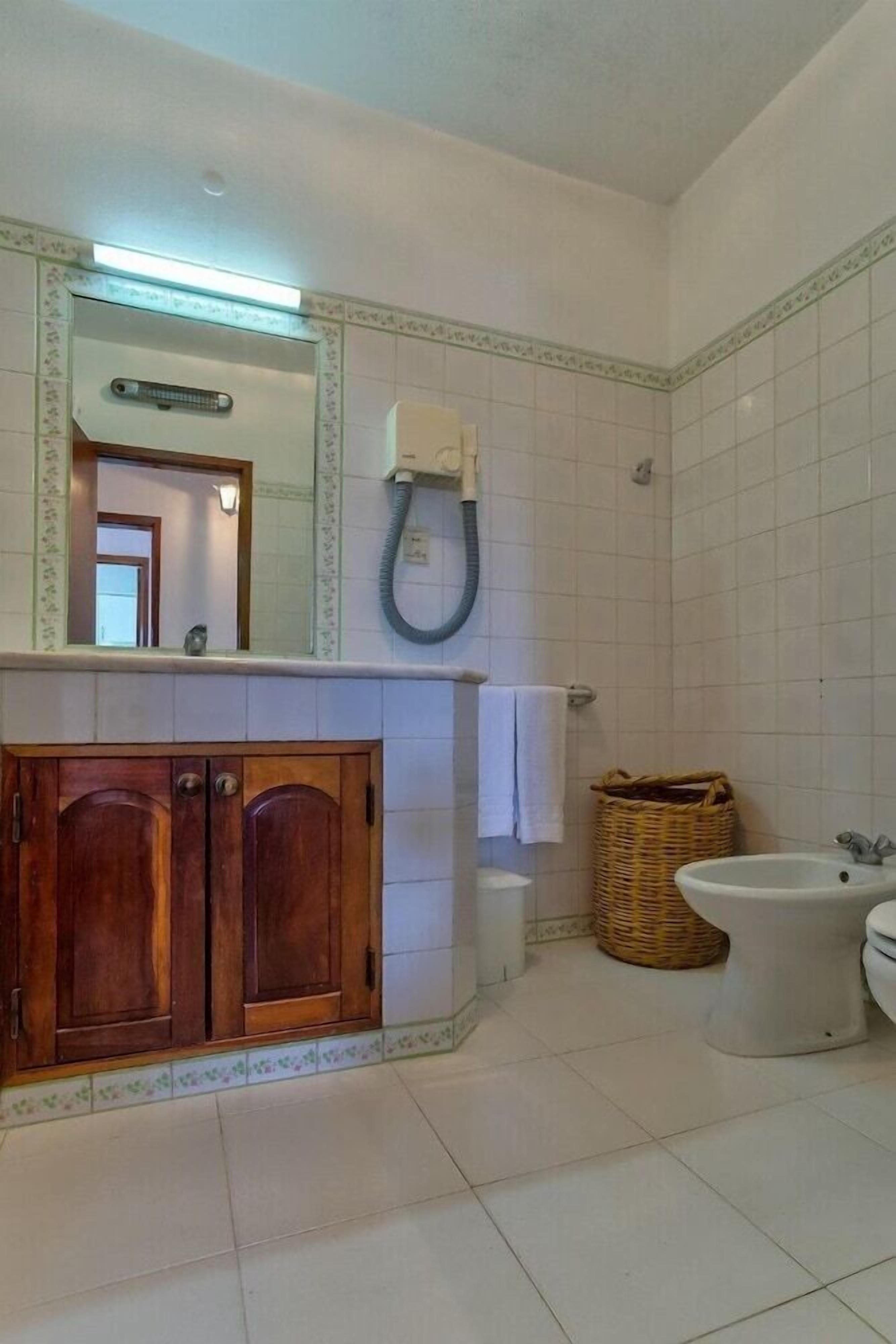 A bathroom with a wooden vanity, a white sink, a bidet, and a mirror above the vanity.