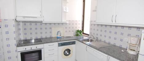 A compact kitchen with white cabinets, a built-in oven, a washing machine, and a coffee maker.