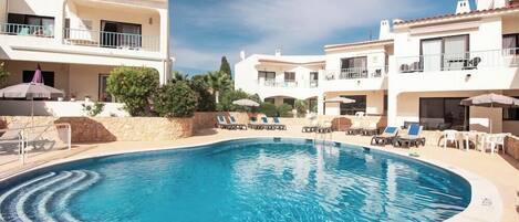 A swimming pool surrounded by lounge chairs and umbrellas, with a clear sky above.