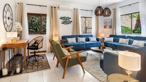 Ein modernes Wohnzimmer mit einem blauen Sofa, grünen Sesseln, einem Holztisch und einem Essbereich mit Tisch und Stühlen.