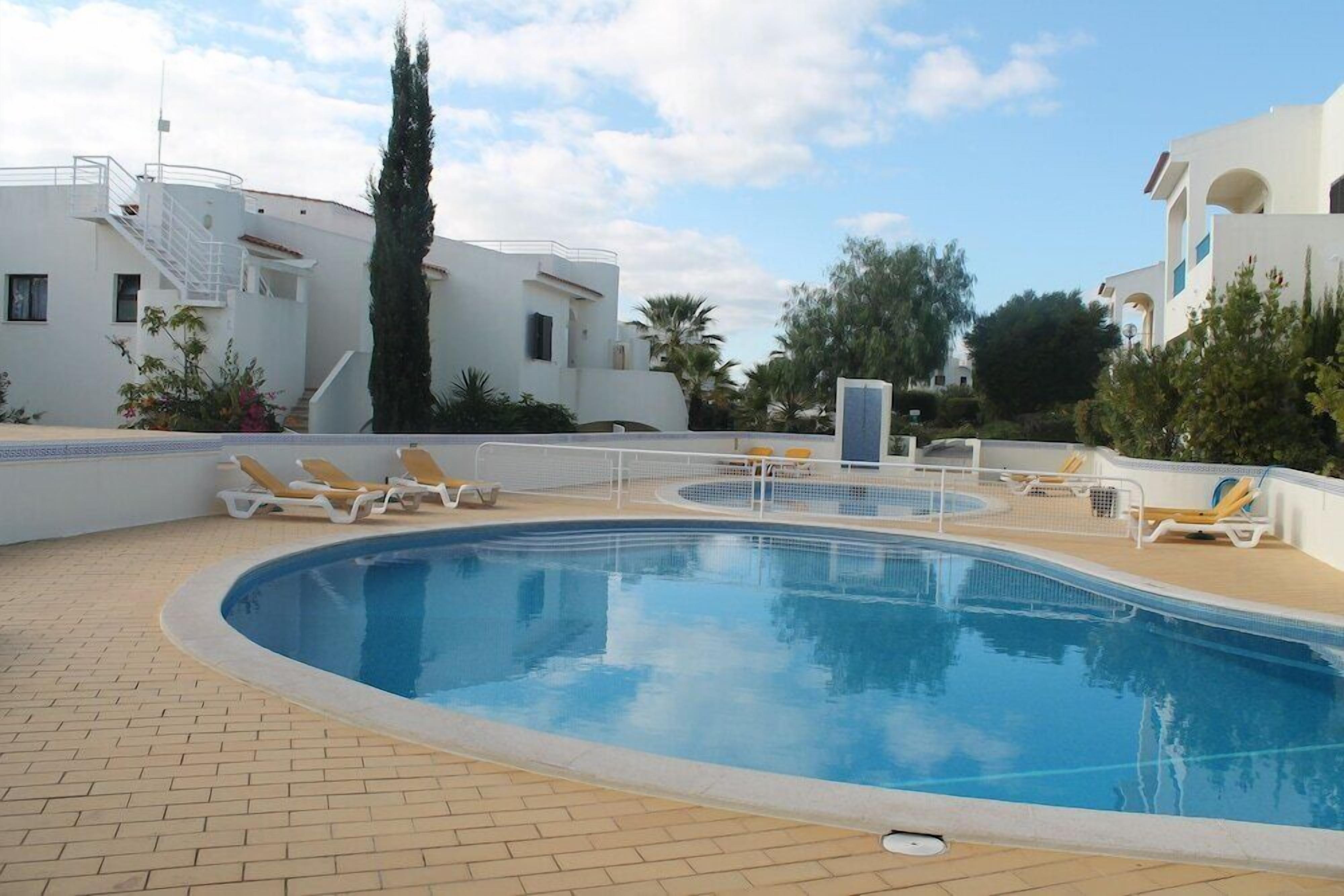 A swimming pool with lounge chairs, a staircase, and white buildings with balconies.