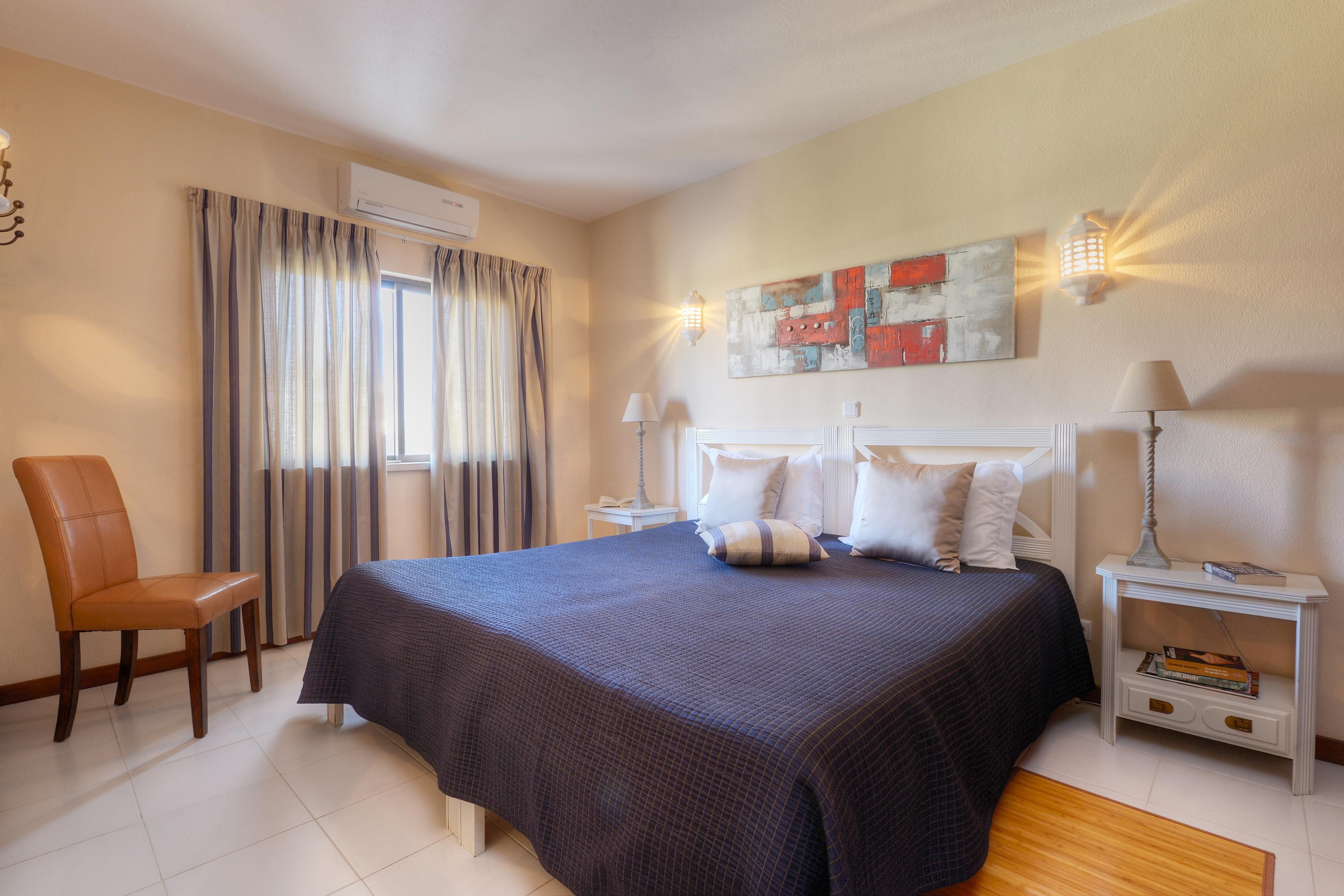 A hotel room with a bed, a chair, a nightstand, a lamp, and a painting on the wall.
